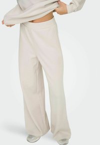 Beige brede sweatpants med en glat tekstur og elastisk talje, parret med lysefarvede træningssko.