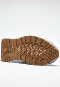 Reebok-sula i brunt gummi med texturerat grepp, med ett zigzag-mönster och logotyp. Ljusblå överkant synlig.