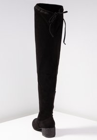 Bota negra por encima de la rodilla en suave ante. Presenta una apertura atada y un tacón grueso con acentos de brillo. Textura suave, diseño elegante.