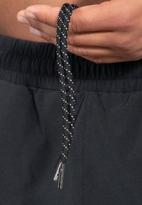 Cuerdas de tiro con un patrón en blanco y negro sujetas por una mano, con puntas de metal, diseñadas para su uso en prendas o accesorios.