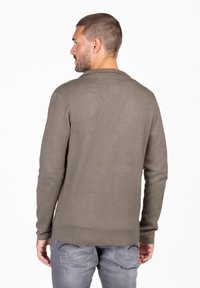 Bruine gebreide trui met lange mouwen, een ronde halslijn en een relaxed fit, gecombineerd met vervaagde grijze jeans. Geen zichtbare patronen of versieringen.