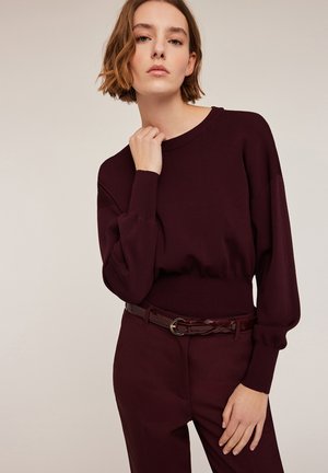 Bordeaux gebreide trui met een ronde hals en pofmouwen, gecombineerd met hoge taille broeken en een glanzende bordeaux riem.