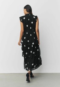 Juoda maksi suknelė su taškeliais, permatomu sluoksniuotu dizainu, raukšlėmis ant pečių ir prigludusia juosena. Dėvima su juodais aukštakulniais bateliais.