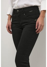 Svarta denimjeans med en figursydd design, hög midja, framfickor, silverdetaljer och en subtil logotypakcent. Slät textur och klassisk stil.