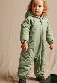 Groene gewatteerde sneeuwpak met een capuchon, versierd met kleine dierenpatronen en elastische manchetten. Ritssluiting en stevige zwarte schoenen.