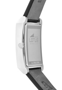 Fond de montre rectangulaire en métal argenté avec logo « Lotus », bracelet en cuir noir et couronne latérale avec symbole gravé.