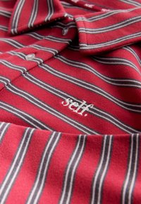 Punaste triipudega polosärk, millel on kitsad valged ja hallid triibud, pehme kangast tekstuur ning rinnal tikitud kiri "self.".