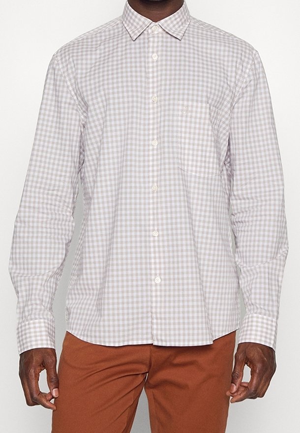 Homme portant une chemise à manches longues à carreaux gris clair et blancs avec poche poitrine, associée à un pantalon couleur rouille.