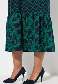 Laivastonsininen mekko, jossa on vihreä saniaiskuvio, ja pleatattu helma. Yhdistettynä laivastonsinisiin mokkanahkakorkokenkiin. Keskittyminen lehvistön yksityiskohtiin ja tekstuuriin.