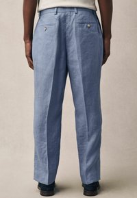 Pantalones de lino azul claro con un ajuste relajado, que cuentan con dos bolsillos traseros con cierres de botón y una textura suave.