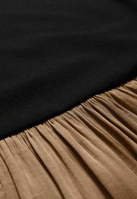 Zwarte bovenzijde met een gladde textuur, gecombineerd met een geplooide beige onderkant, die zachte stof en contrast tussen materialen laat zien.