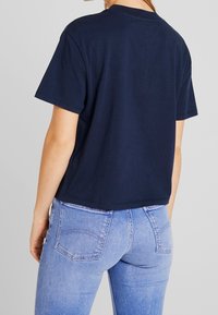 Marineblå bomullströja med korta ärmar, rak skärning och rund halsringning, ihop med ljusblå jeans med bakfickor.