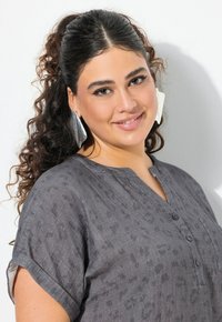 Camicia con stampa leopardata grigia, con scollo a V e maniche corte, dotata di bottoni e tasca frontale, realizzata in un tessuto morbido e strutturato.