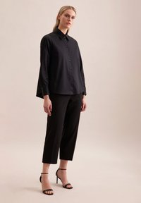 Schwarz, knopfgebundenes Hemd mit lässiger Passform und langen Ärmeln, kombiniert mit maßgeschneiderten schwarzen Hosen und verzierten schwarzen High Heels.