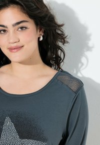 Mørkegrå langærmet t-shirt med stjernedesign i rhinsten og mesh-detaljer på skuldrene. Glat stofstruktur, rund halsudskæring.