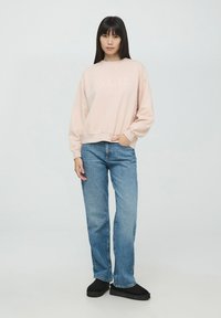 Jasnoróżowy sweatshirt z napisem "AMOUR", luźny krój, ściągacze na mankietach i dole. Połączony z niebieskimi prostymi dżinsami i czarnymi butami na platformie.