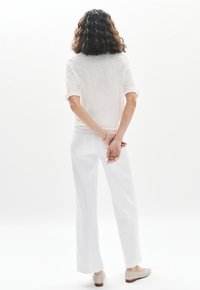 Top de lino blanco con mangas enrolladas, combinado con pantalones anchos blancos. Textura suave, esquema de colores neutros, finalizado con zapatos de lona beige.