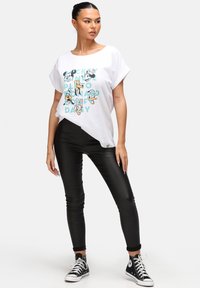 Hvid kortærmet T-shirt med tryk af tegneseriefigur, parret med sorte leggings og sorte høj-top sneakers. Glat tekstur, afslappet pasform.