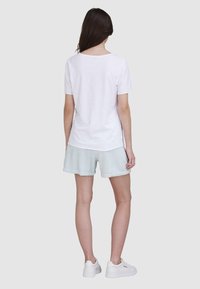 T-shirt blanc à manches courtes avec un col légèrement arrondi, associé à un short vert clair et des baskets blanches, vu de dos.