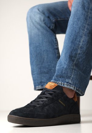 Donkerblauwe suède sneakers met een bruine leren accent op de boord, voorzien van platte veters en textuur zijpanelen. Rubberen zool.