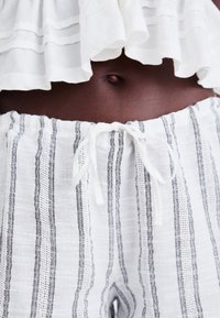 Pantalons rayés légers et blancs avec des lignes noires, une taille élastique et un cordon de serrage en haut.