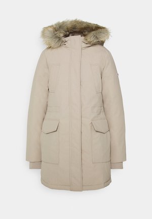 Manteau d'hiver beige mi-cuisses avec capuche doublée de fourrure, fermeture éclair devant recouverte par un rabat, deux poches poitrine et deux grandes poches à rabat près de la taille.