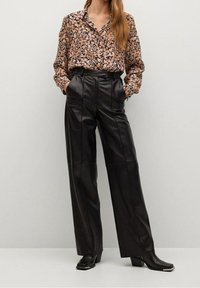 Blouse à motif floral en tissu doux, associée à un pantalon en cuir noir taille haute avec des coutures visibles et une silhouette évas ée.