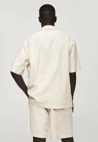 Hellbeiges Kurzarmhemd und passende Shorts aus einem glatten, strukturierten Stoff mit einem lockeren Schnitt und einfachem Kragendesign.