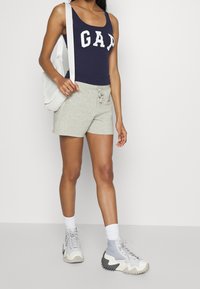 Débardeur marine avec le lettrage blanc "GAP", shorts gris avec cordon de serrage, et baskets chunky gris et blanc, accompagnés d'un sac texturé blanc.