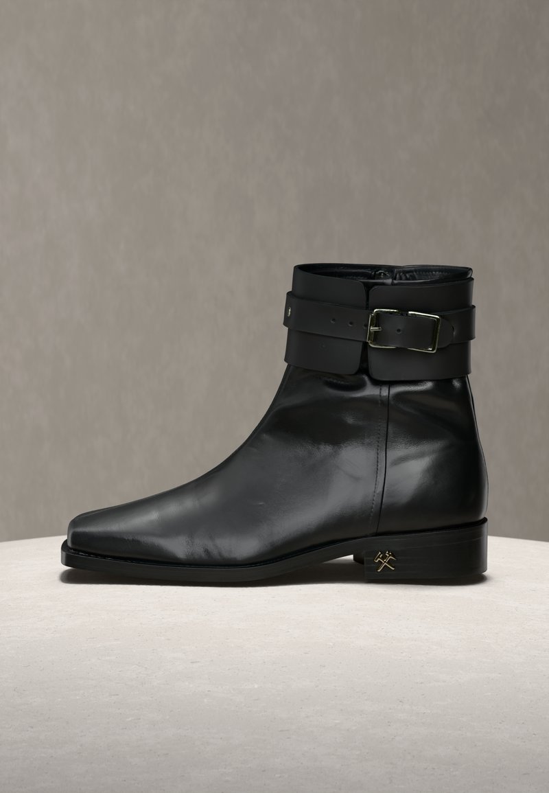 Stivaletto nero in pelle con punta appuntita, ampia fascia decorativa con fibbia argentata sulla parte superiore e piccolo logo dorato sul tallone.