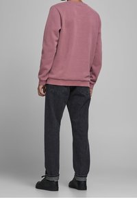 Felpa rosa con collo rotondo, abbinata a pantaloni in denim grigio scuro. I tessuti sembrano morbidi e leggermente strutturati. Scarpe nere completano il look.