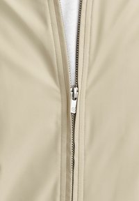 Bežna zip-up jakna z gladko teksturo in srebrnim zadrgo, ki prikazuje bližnji pogled na območje zadrge in podrobnosti tkanine.