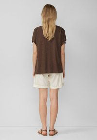 Bruine korte mouwen top met een relaxte pasvorm, gecombineerd met crèmekleurige shorts. De shorts hebben opgerolde mouwen en zijn gemaakt van lichtgewicht stof.