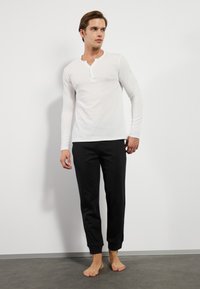 White long-sleeve top with a round neckline and a button placket, paired with black tapered sweatpants featuring ankle cuffs.