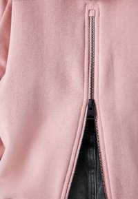Weicher rosa Stoff, teilweise geöffnet, um darunter schwarzes strukturiertes Material mit sichtbaren silbernen Reißverschlusszähnen und Zuglasche zu zeigen.