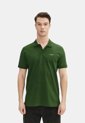 Polo shirt verde scuro in cotone, con colletto a tre bottoni e un piccolo emblema ricamato sul lato sinistro del petto. Maniche corte.