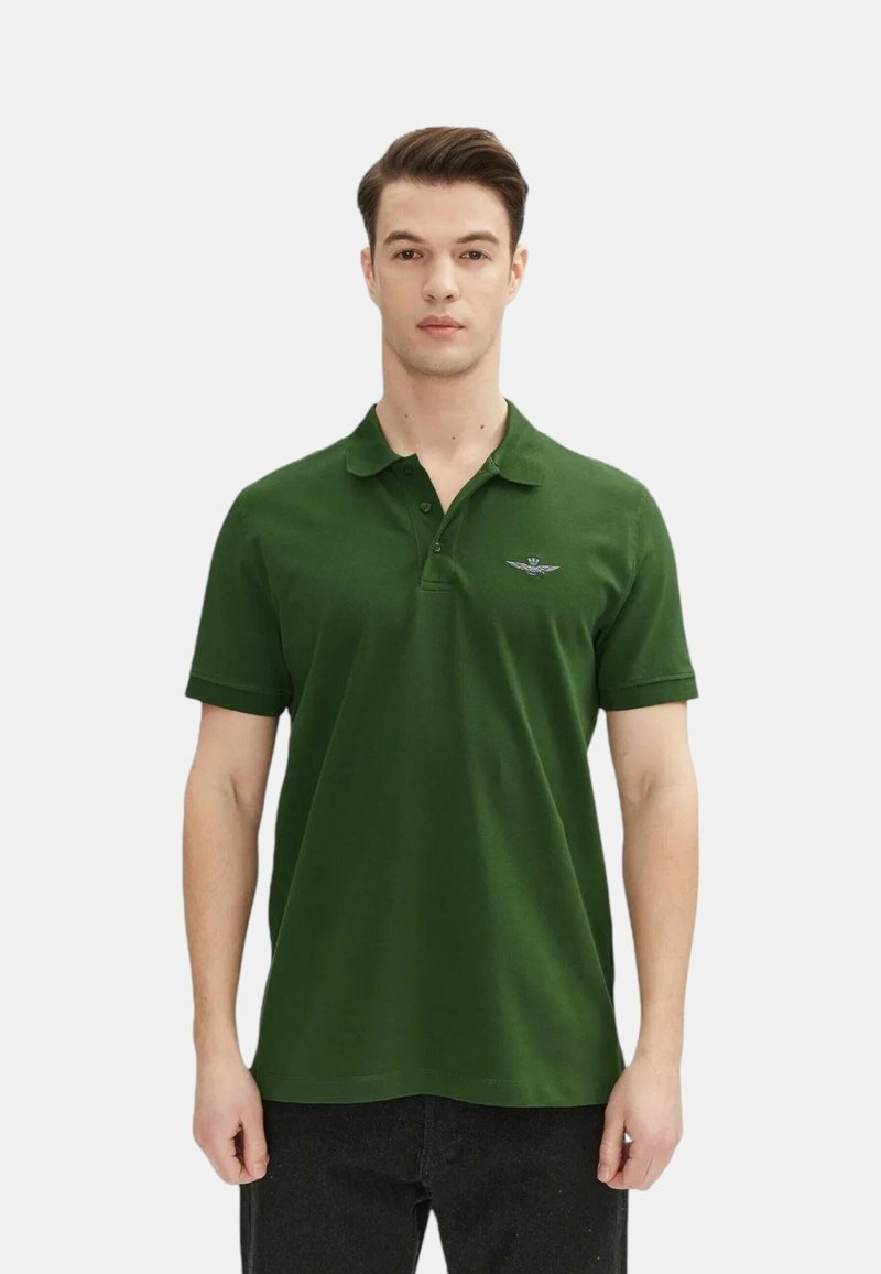 Polo shirt verde scuro in cotone, con colletto a tre bottoni e un piccolo emblema ricamato sul lato sinistro del petto. Maniche corte.