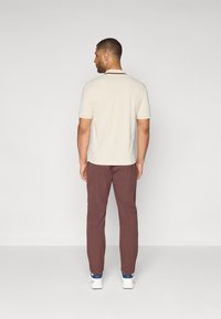 Kratki bež polo majica s tamnim ovratnikom, uparena s burgundskim hlačama. Model nosi bijele tenisice. Čist, prilagođen dizajn.