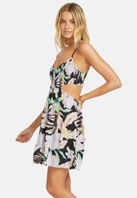 Robe florale avec un corsage ajusté et un détail découpé. Présente un fond noir, des fleurs aux couleurs pastel, des bretelles réglables et une jupe évasée.