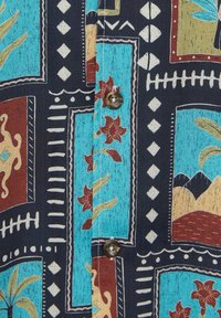 Tissu de chemise boutonnée avec motifs géométriques et floraux en bleu sarcelle, rouge, jaune et noir, présentant des formes carrées et losanges.