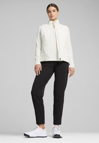 Quilted white vest with a high collar, worn over a light top, paired with black pants and white sneakers. Smooth texture and tailored fit.