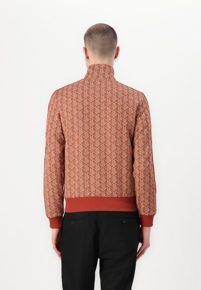 Veste bomber à motif rouge et beige avec un col montant, des poignets et un bas côtelés, présentant un design géométrique répétitif.