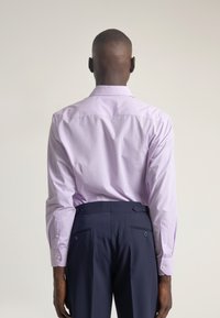Camisa de manga larga morado claro con cuello clásico y costuras visibles, combinada con pantalones oscuros de color navy que tienen dos bolsillos traseros.