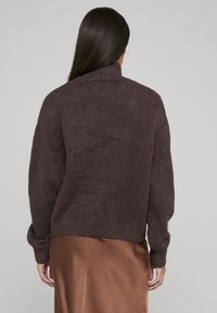 Bruin, grofgebreide trui met een hoge kraag en geribbelde manchetten, gecombineerd met een gladde, bronzen satijnen rok. Eenvoudig en gestructureerd ontwerp.