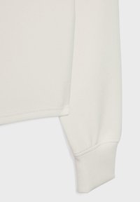 Manche longue de chemise couleur crème avec poignet côtelé, montrant des coutures détaillées et une texture de tissu lisse.