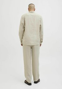 Camisa de lino color beige claro con mangas largas y un pliegue en la parte trasera, combinada con pantalones de lino a juego. Textura suave y corte holgado.