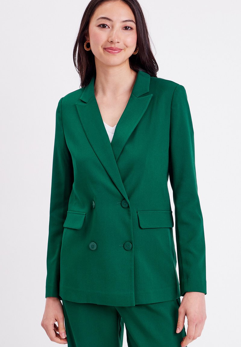 Green double-breasted blazer with notched lapels, two front pockets, and button accents. Smooth fabric texture, tailored fit, and structured design.