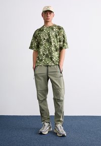 Grønternet kortærmet skjorte parret med lys grønne cargo-bukser og grå-blå sneakers. Outfittet byder på en afslappet pasform og lynlåse.