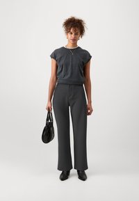 Dark gray short-sleeve t-shirt with rolled cuffs, paired with high-waisted, wide-leg dark slacks. Holds a small black bag. Black shoes.