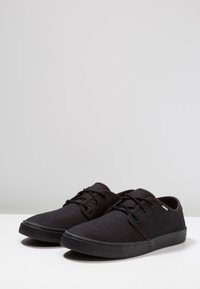 Mustat kangas nauhakenkä, jossa on teksturoitu pinta, pyöreä kärki ja kumipohja. Ominaisuuksiin kuuluu kontrastivärit nauhat ja hillitty logo painatus.